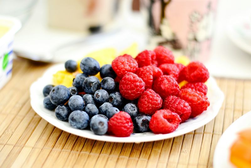 A white plate with a variety of blueberries, raspberries, and pineapple on a wooden background.